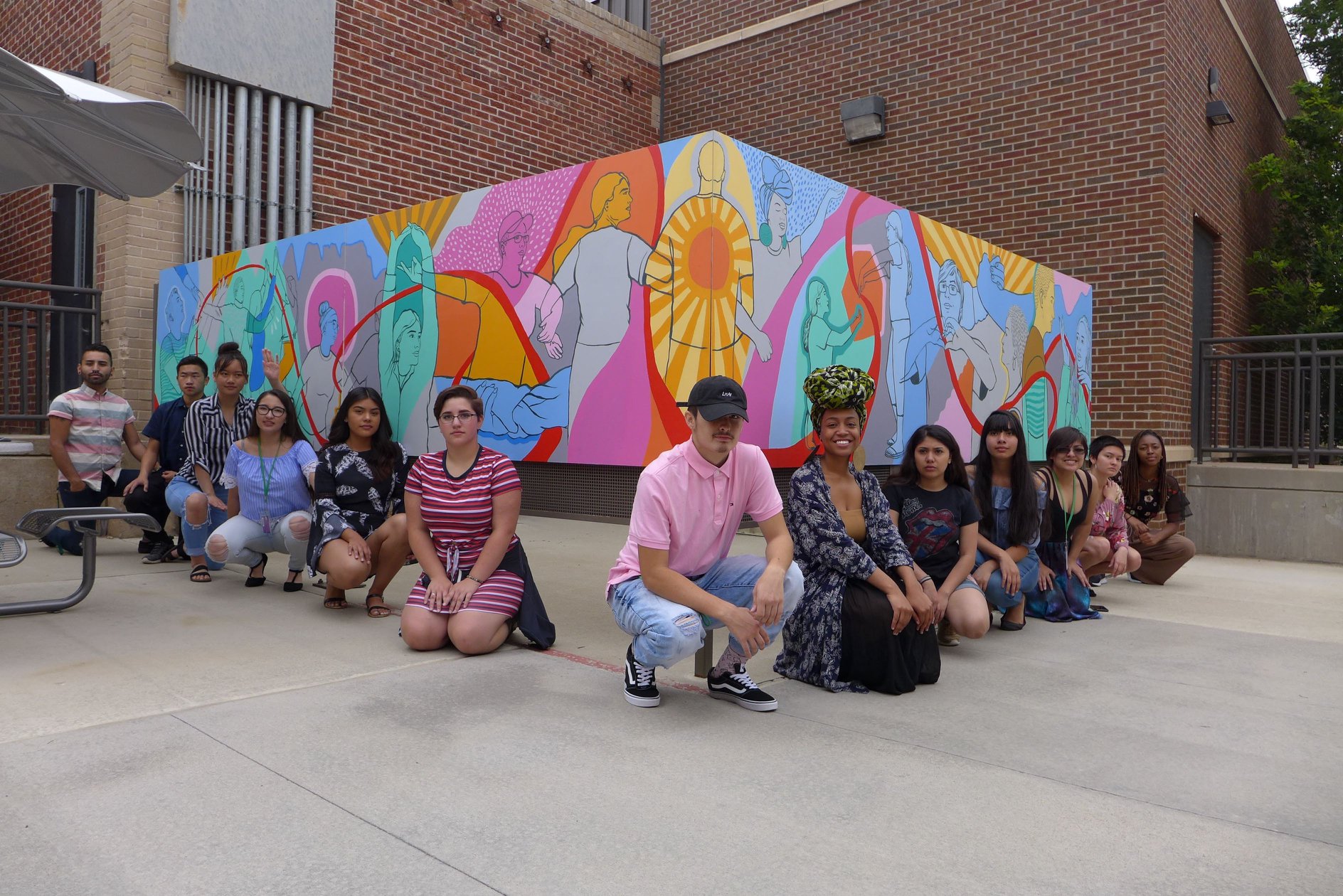 Social Justice Thru the Arts student participants kneeling in front of their collaborative mural