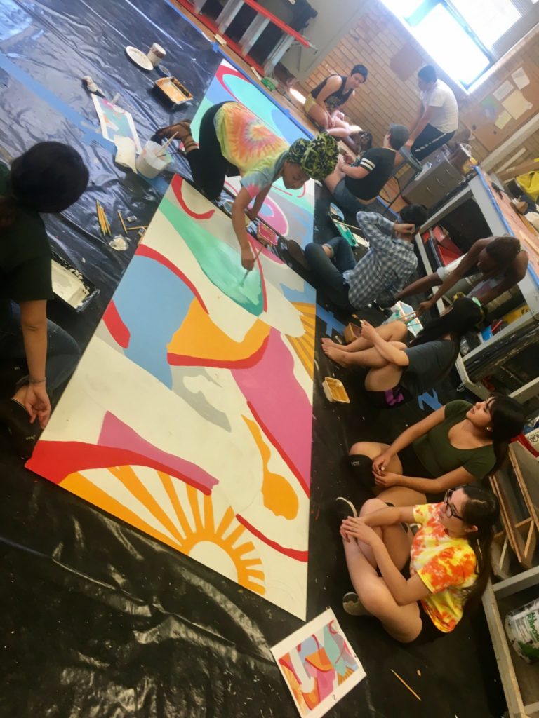 Student gather in the set design classroom in the UCA to paint their mural during SJTA