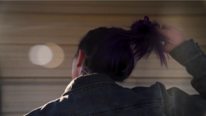 A woman facing away from the camera pulls on her ponytail