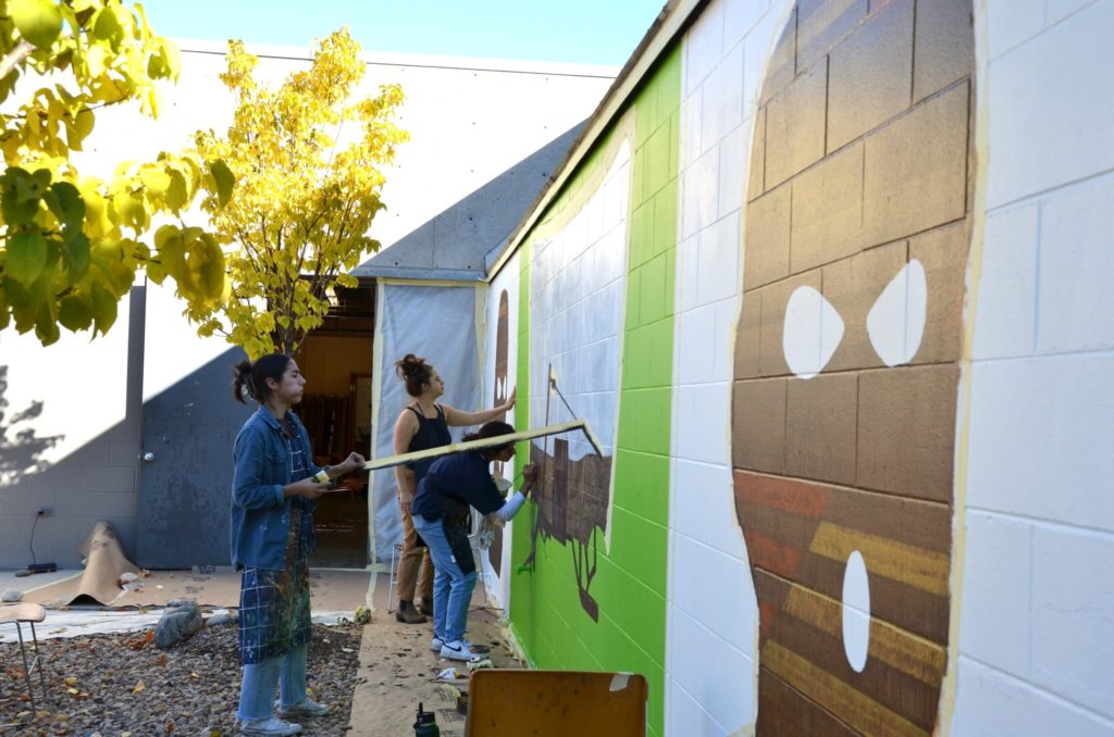 Visual arts graduate student removing tape guidelines from wagon section on mural. Credit: Ellie Crowley.