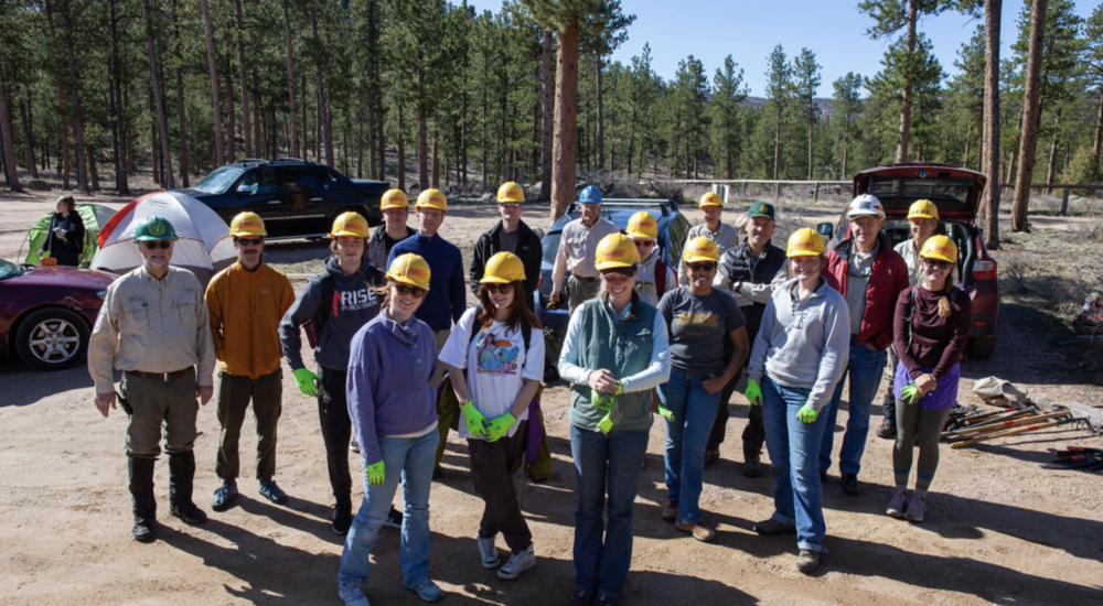 Group of students and professors with hard hats and shovels grouped together, smiling