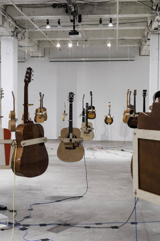 A large, white room with dozens of guitars and other stringed instruments suspended from the ceiling.